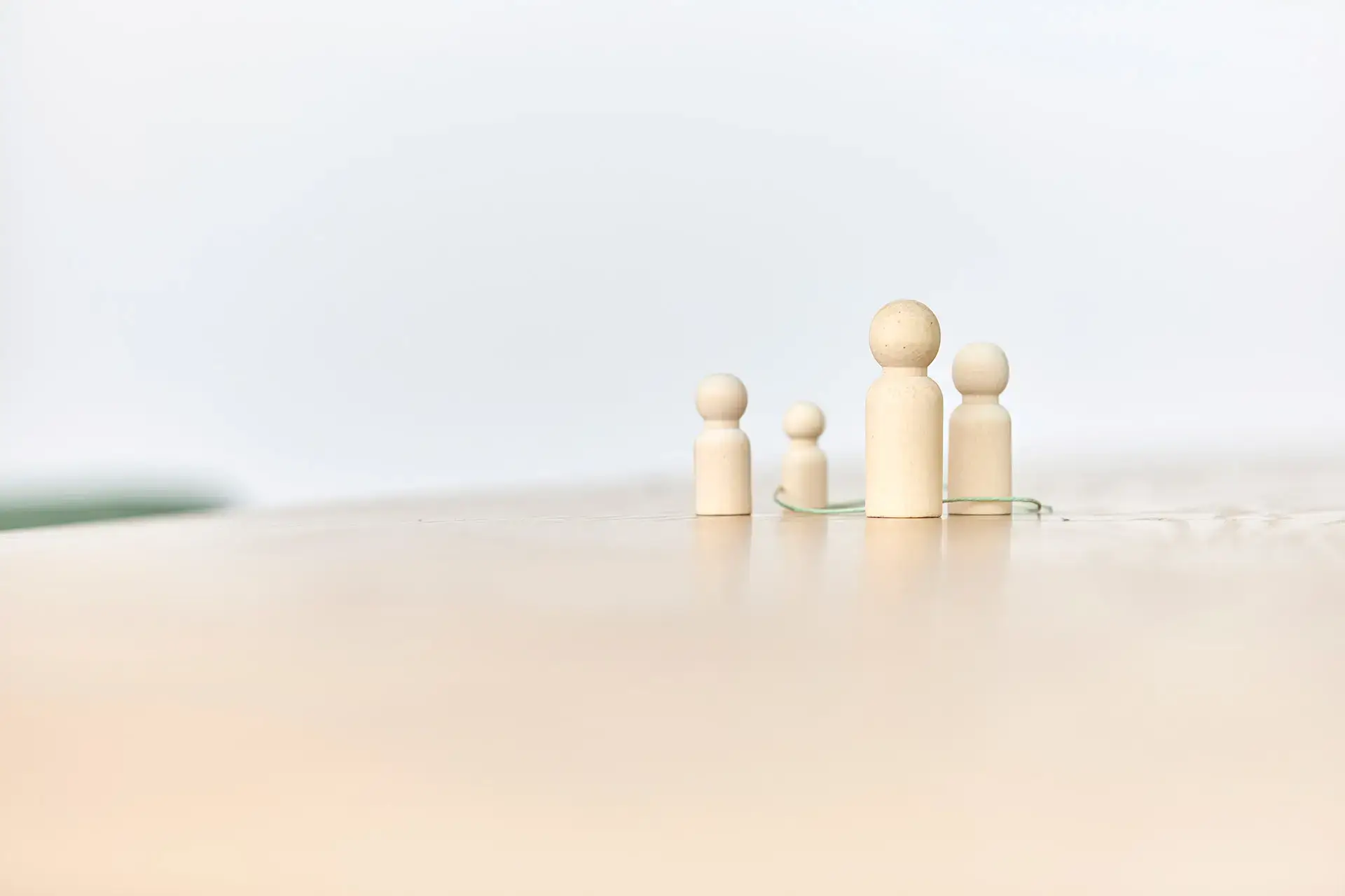 Helle Holzfiguren in sanften Pastelltönen stehen nah beieinander und symbolisieren Paar- & Familientherapie, Familie und systemische Beziehungen.