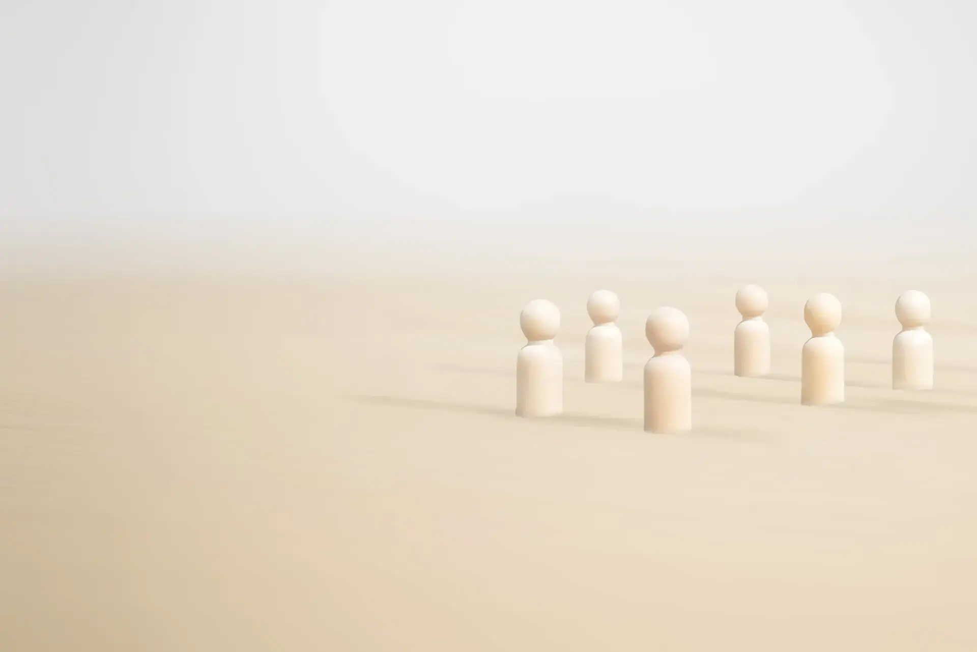 Helle, minimalistische Holzfiguren stehen in lockerer Gruppe auf sandfarbenem Untergrund und veranschaulichen Teamsupervision im sozialen Bereich.